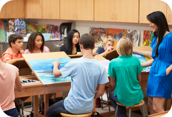 Teens gathered around a table with a piece of artwork in progress while a teacher looks on