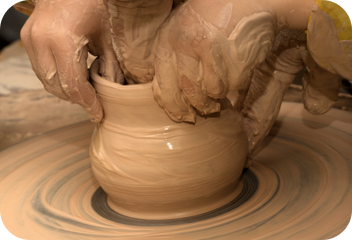 Two hands work a cup on a potter's wheel.