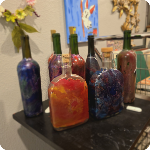 Wine and liqour bottles brightly painted with metallic paints in red, orange, green, blue, and purple.