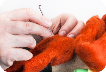 Two hands work on an animal made of red felt with a large felting needle.